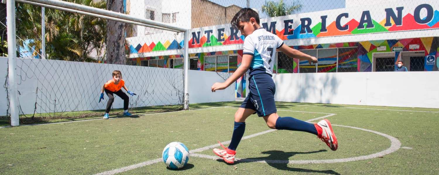Niños jugando fútbol en cancha de fútbol en colegio interamericano.
